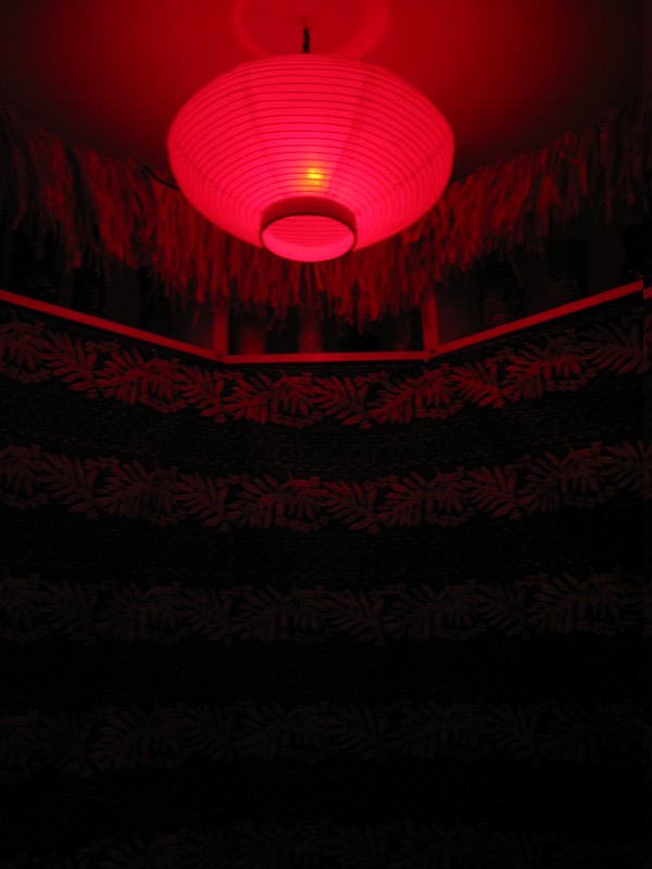 This red light sits in the corner. Below it sits one of two Hey-Wake tables with menus, postcards, and other treasures from Tiki sites across the country.
