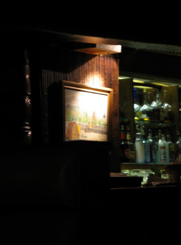 The painting at the left edge of the bar. There's a carved Tiki pole to the left of the painting.